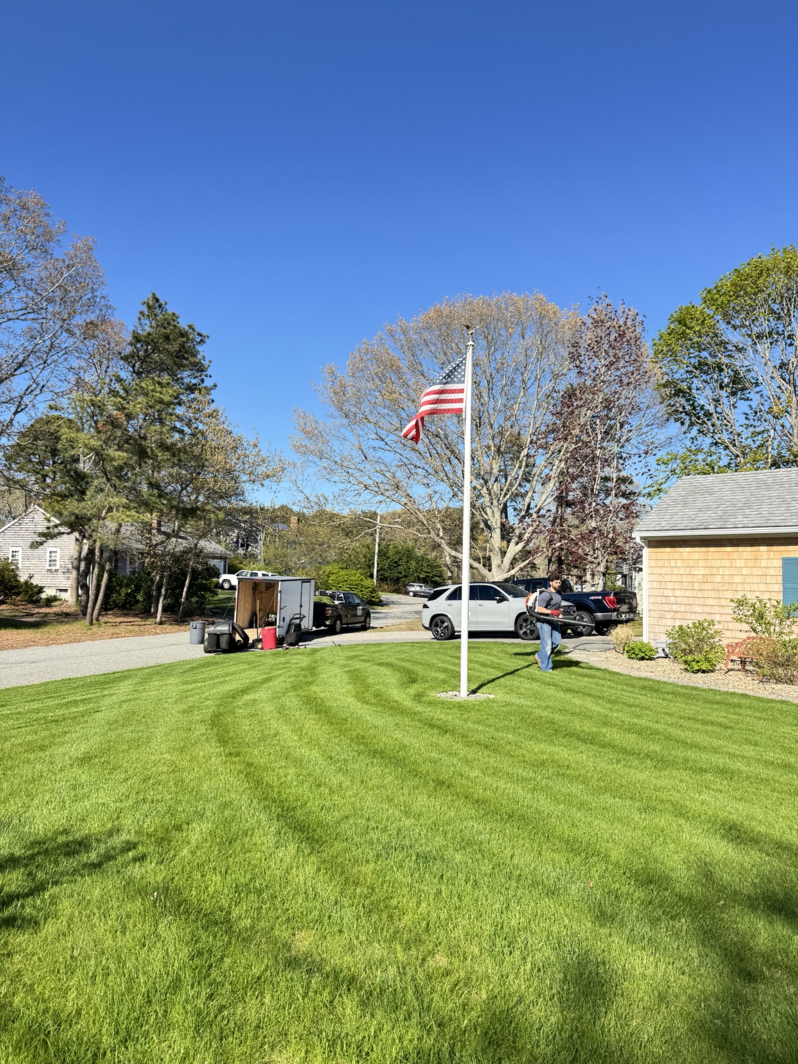 Crew maintaining a bright green lawn beneath an American flag
